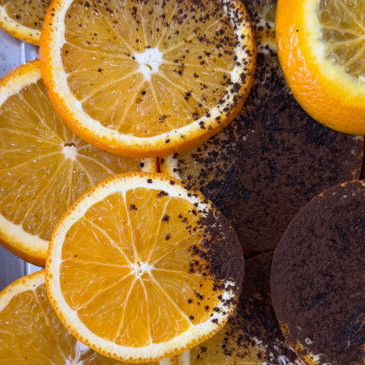 Close-up of orange slices and dark chocolate pieces arranged together, with some orange slices dusted in dark powder.